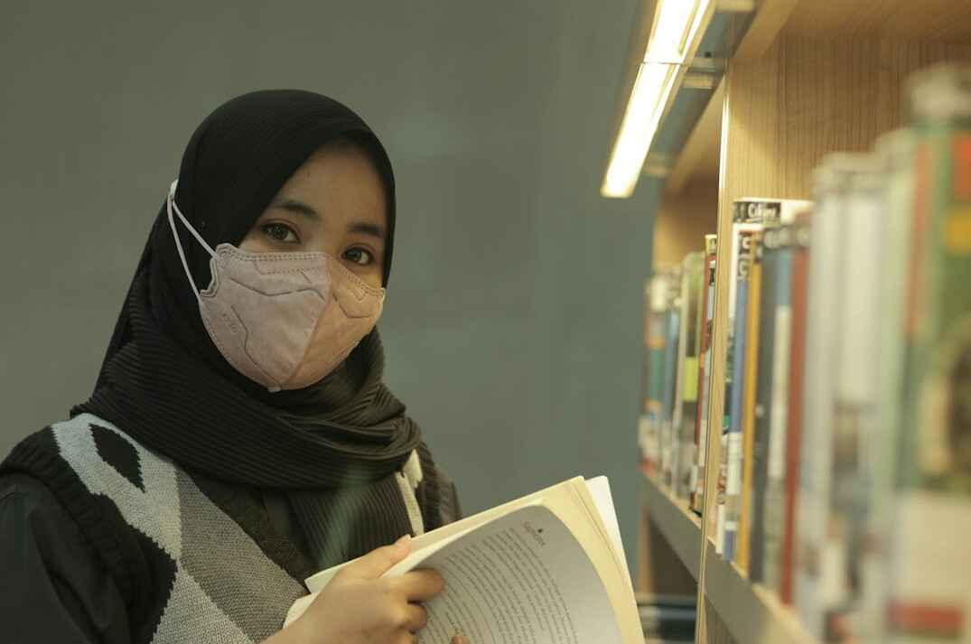 Young Malaysian student studying programming on a laptop in a library